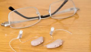A close-up of a hearing aid next to a pair of glasses